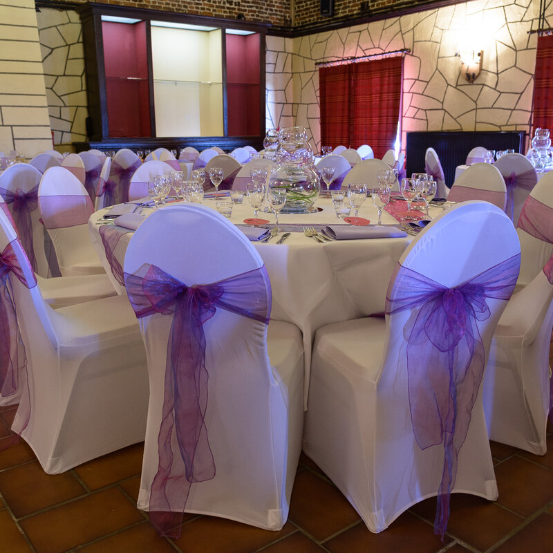 Salle de mariage décorée avec housses de chaises et nœuds violets au domaine Le Scaubecq